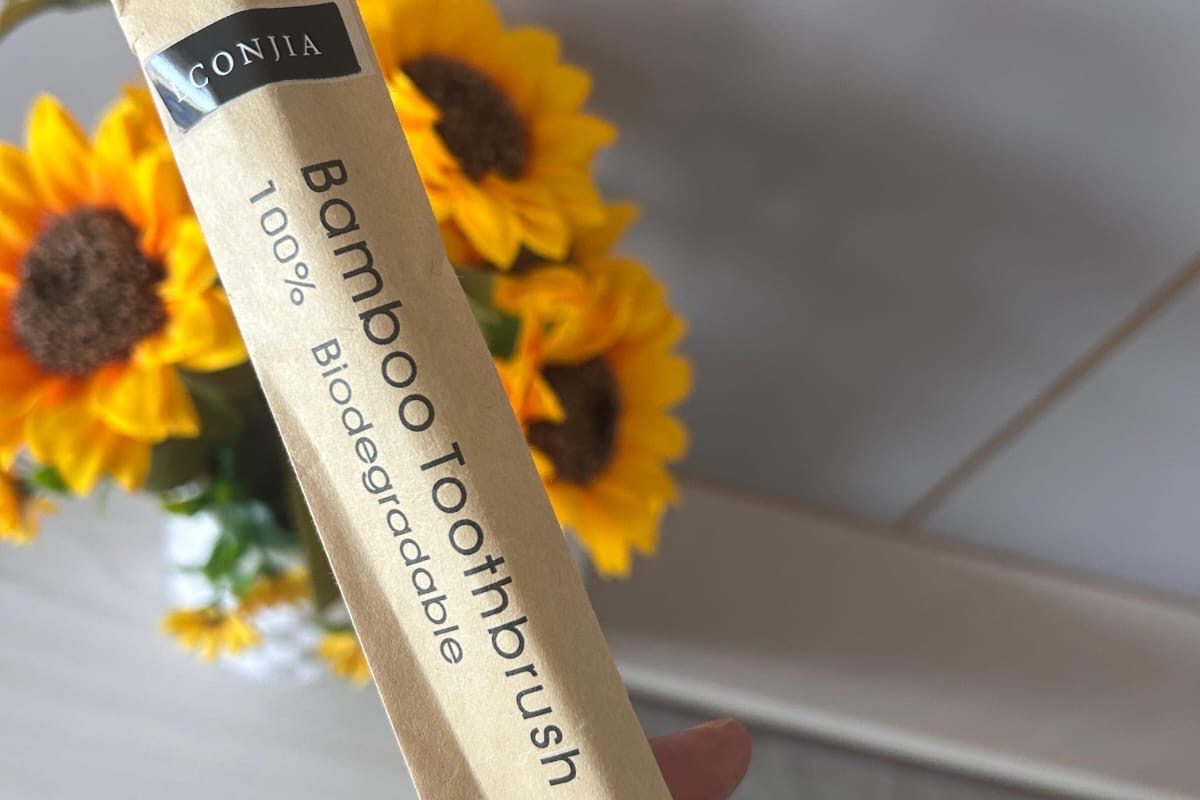 A bamboo toothbrush in kraft paper packaging, held up in front of sunflowers.